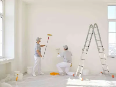Deux peintres en train de repeindre un mur blanc dans une pièce vide.