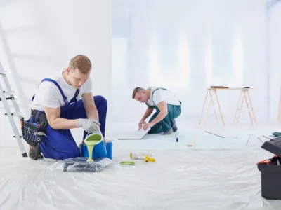 Deux peintres préparant le sol avant des travaux de peinture intérieure.