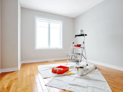 Pièce vide préparée pour des travaux de peinture avec échelle et matériel.