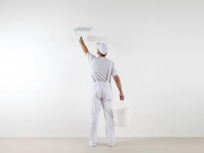 Peintre appliquant de la peinture blanche au rouleau sur un mur.