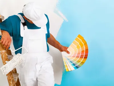 Peintre tenant un nuancier devant un mur bleu en cours de peinture.